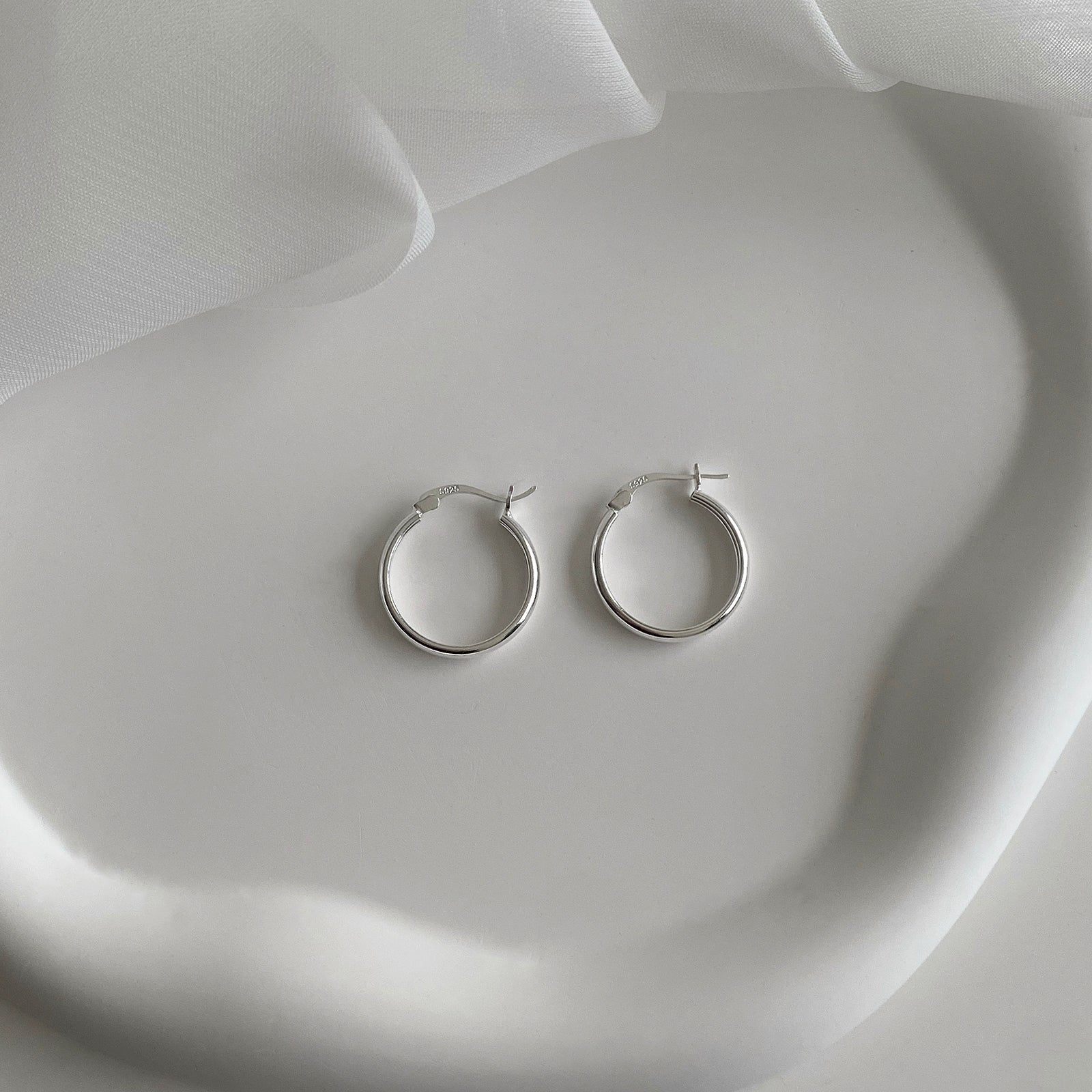 Top view of Jane Hoops 20mm are classic hoop earrings with a latch back for closure. It's made of 925 sterling silver with a shiny smooth finish. Perfect hoop earrings for everyday. Has a S925 stamp on the latch.